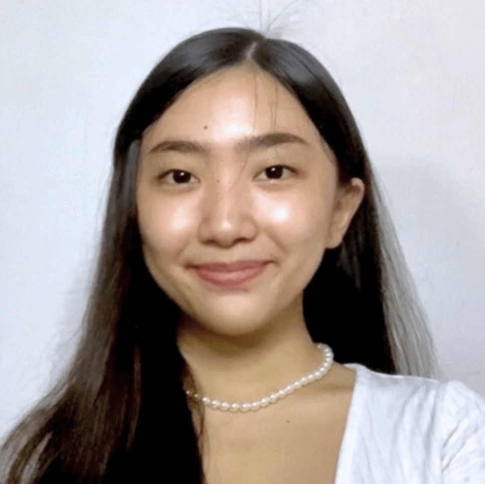 A young woman with long dark hair and a pearl necklace smiles at the camera against a plain white background.